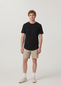 Man wearing a black heritage curved hem luxury t-shirt and beige shorts on a white background