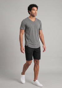 Man in mid 30s wearing grey vneck and black shorts, with white shoes, walking 