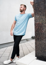 Male model leaning against granite brick in Ten10 Apparel light blue short sleeve curved hem shirt