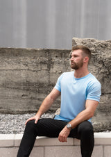 male model sitting on stone ledge in light blue curved bottom shirt