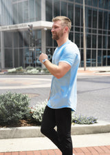 Male model walking across showing a side view in the Ten/10 apparel light blue colored short sleeve crew neck