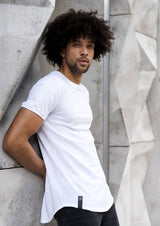 Tall, lightskin, curly haired model, wearing a premium mens white long-lined, fitted t-shirt, leaning on a white, rigid wall in Miami, Florida.