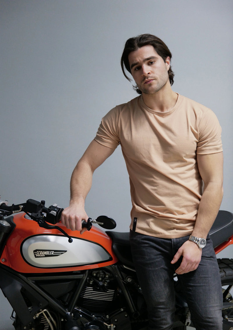 tan longline crew neck t shirt on male model leaning on a ducati motorcycle